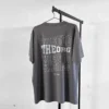 Graues T-Shirt auf an einem Kleiderbügel an einer Kleiderstange. Der Rückendruck ist viermal THEORG in einer wellenförmigen Schrift untereinander. Das zweite THEORG von oben ist weiß ausgefüllt, die anderen haben eine weißen Konturlinie. Darunter steht est. 1989.