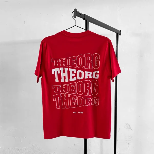 Rotes T-Shirt auf an einem Kleiderbügel an einer Kleiderstange. Der Rückendruck ist viermal THEORG in einer wellenförmigen Schrift untereinander. Das zweite THEORG von oben ist weiß ausgefüllt, die anderen haben eine weißen Konturline. Darunter steht est. 1989.